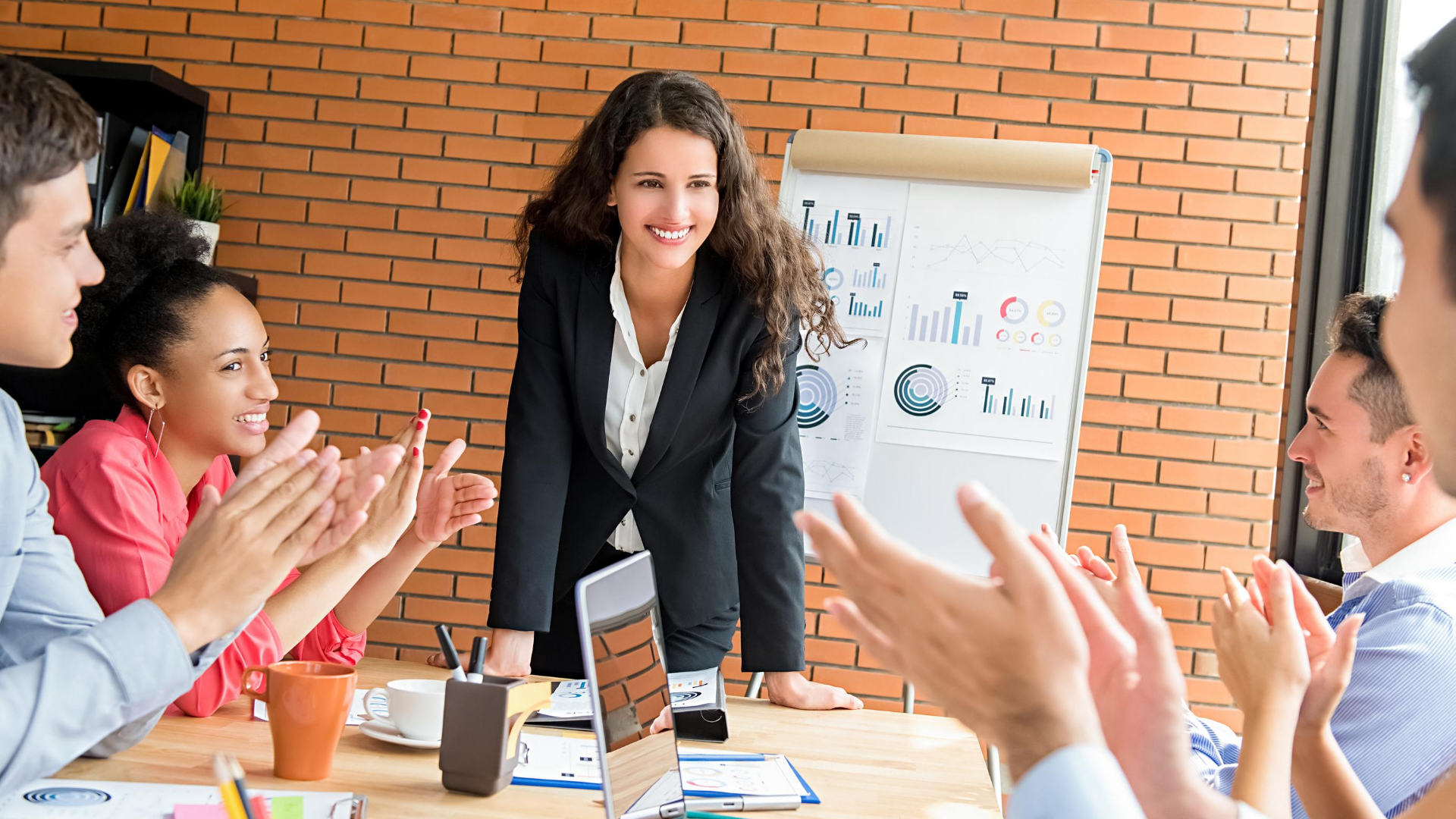 A woman leading a meeting with four team members applauding