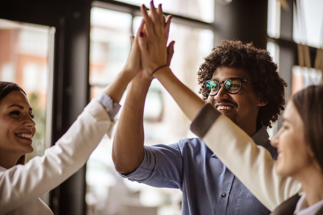 Smiling business team giving a group high five, symbolizing collaboration, trust, and empowerment in a workplace setting
