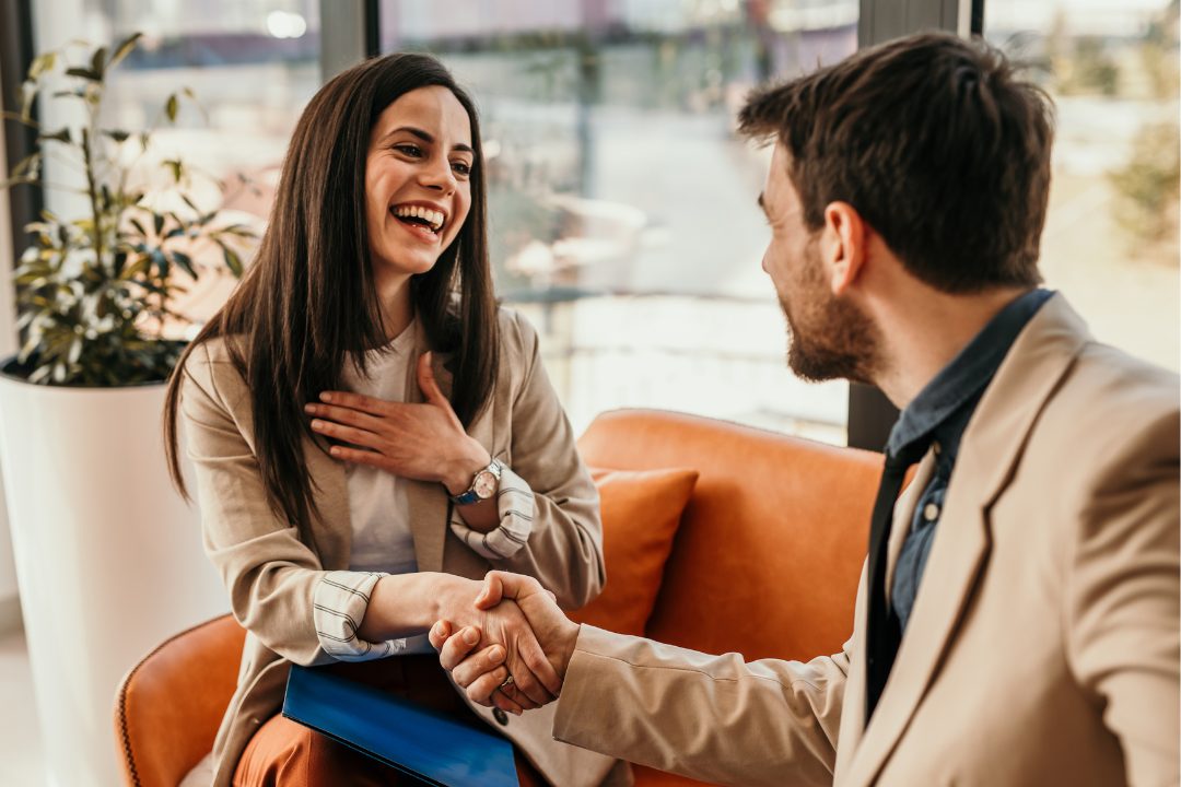 Two professionals shaking hands and reviewing interview notes together in a modern office environment, highlighting intentional hiring and collaborative team growth.